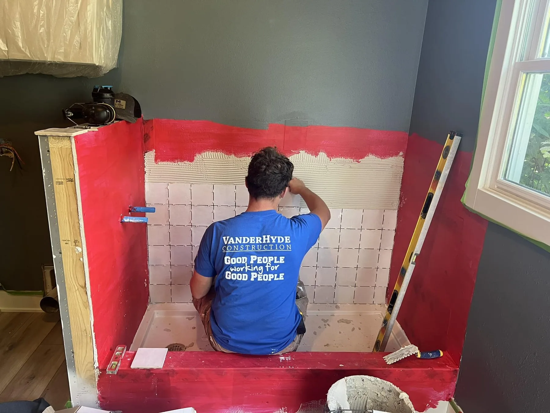 A VanderHyde team member setting tile in a shower over red waterproofing membrane