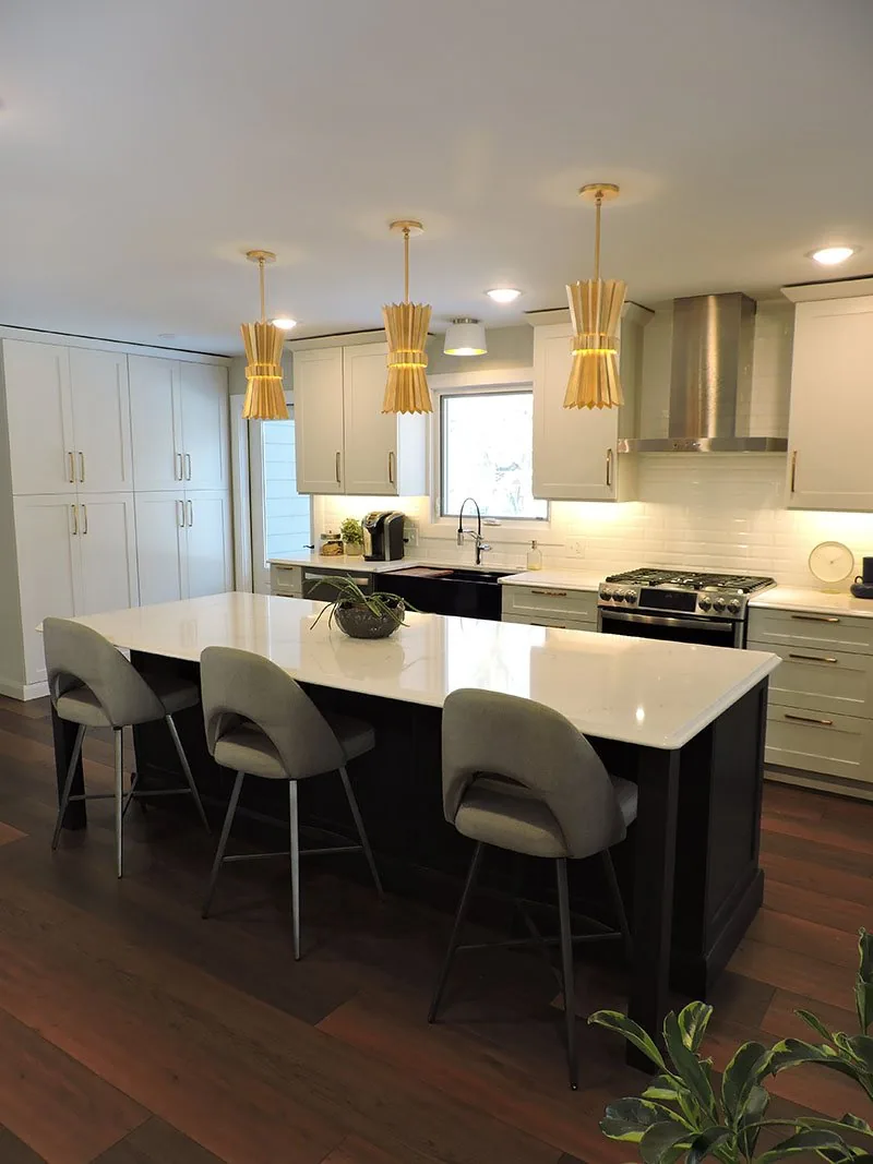 Finished kitchen with a dark island, white quartz counter and brass pendants, built by VanderHyde Construction