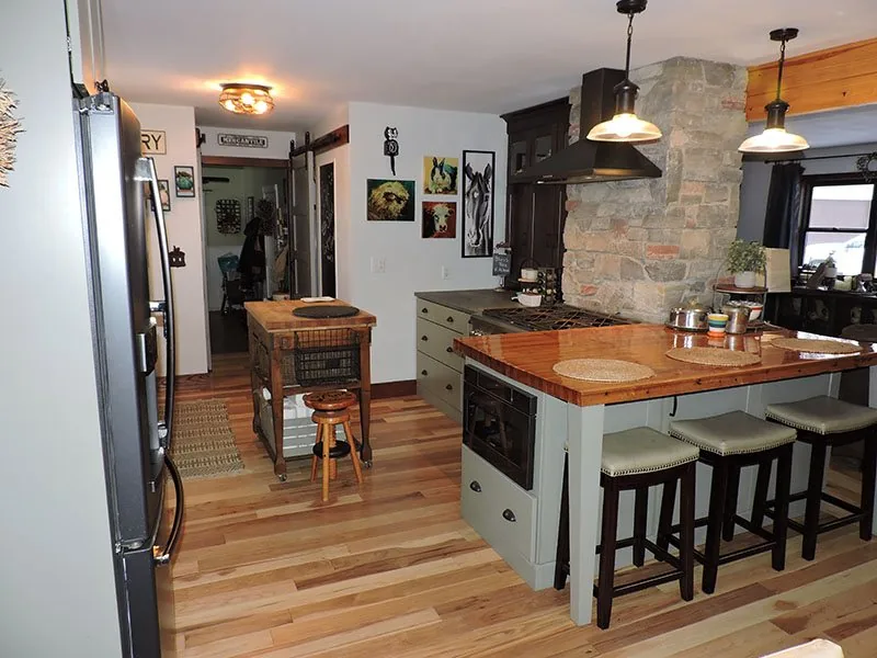 Open kitchen with a butcher block island, sage cabinets and a stone chimney surround